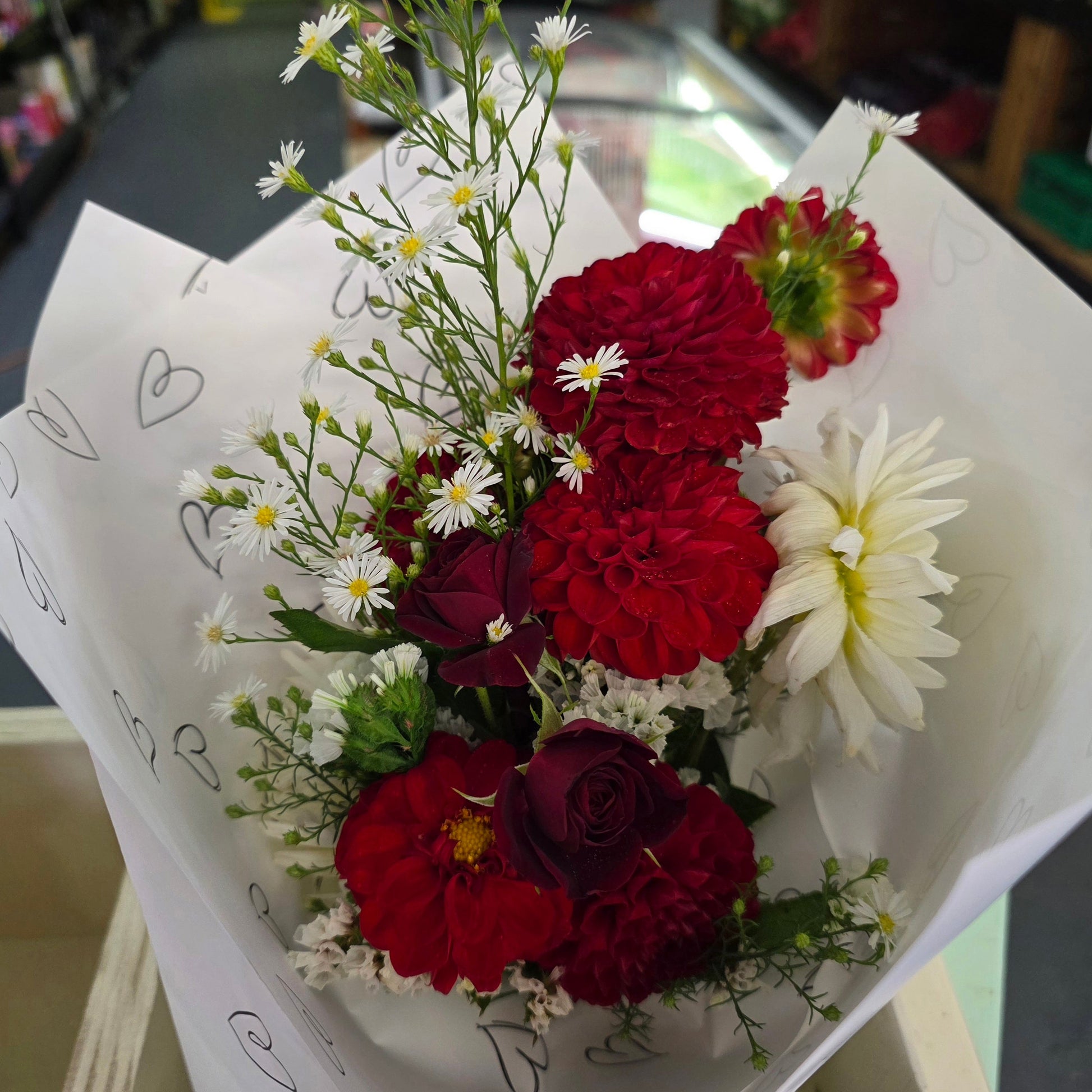 Bouquet of red and white flowers in a white paper wrap with heart designs.