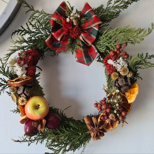 Decorative Christmas wreath with greenery, fruits, and a plaid bow on a white background