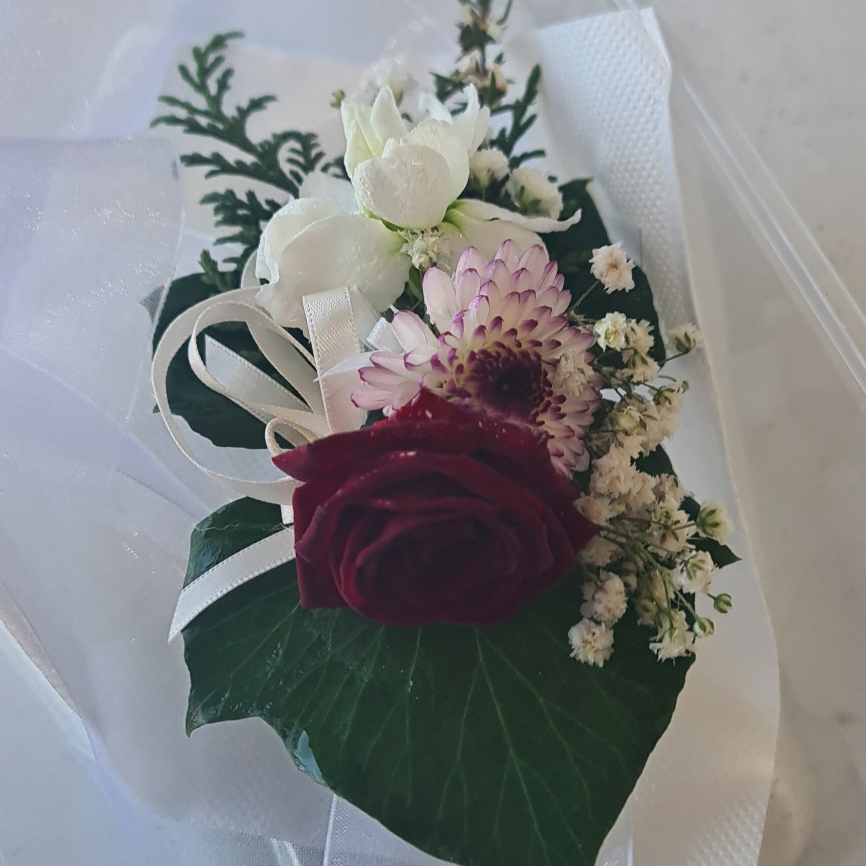 Floral corsage with red rose, white flowers, and green leaves