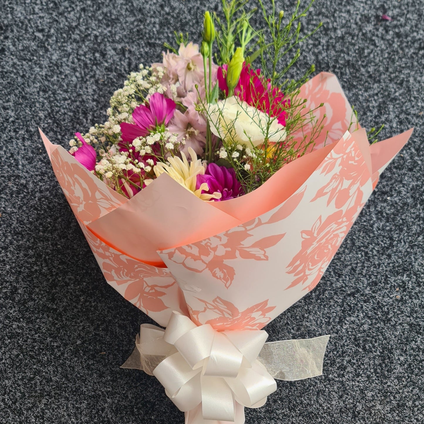 Bouquet of flowers wrapped in pink paper with a white bow on a dark background