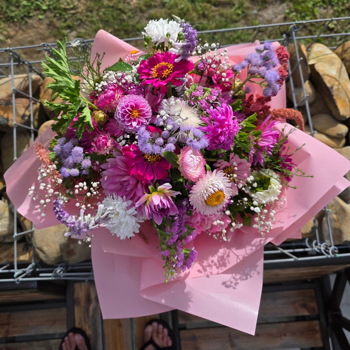 Bouquet of colorful flowers wrapped in pink paper against a rustic background.