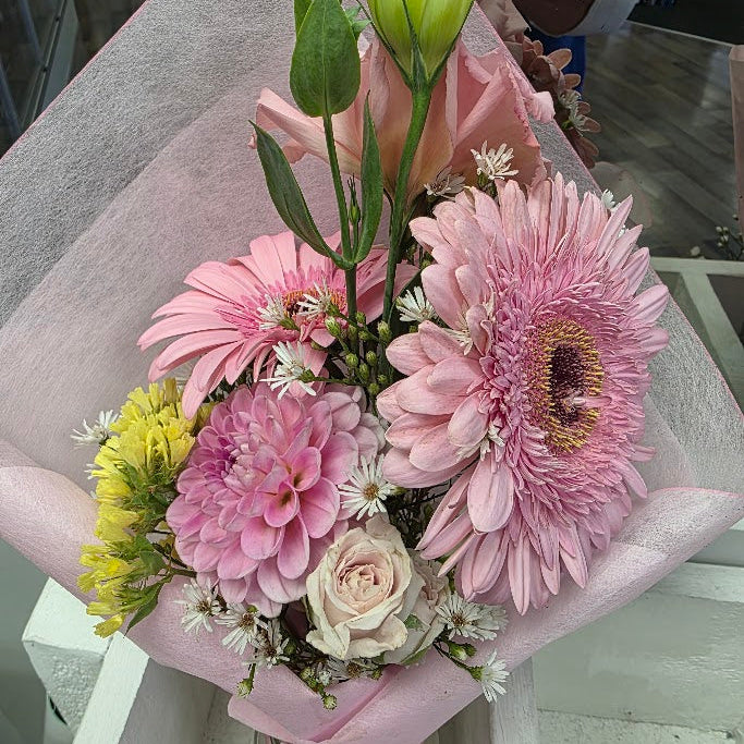 Bouquet of flowers with pink and yellow flowers in a clear vase on a light surface.